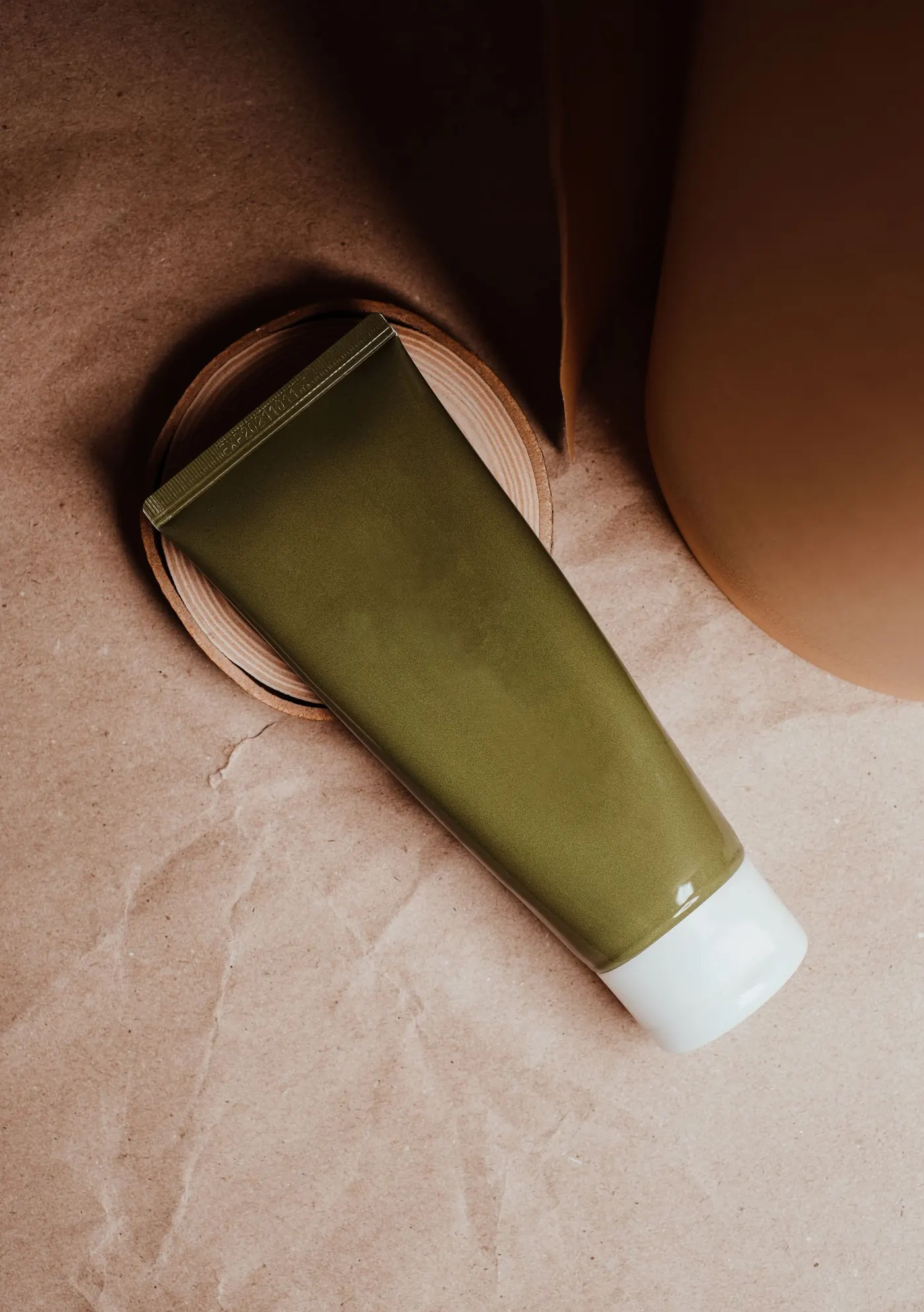 Olive green product tube on tactile paper and ceramic